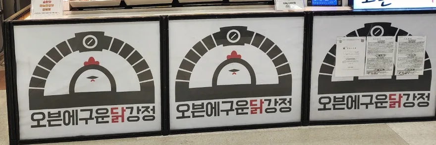 오븐에 구운 닭강정 매장 전면. 오븐 아치 안에 닭이 그려진 브랜드 사인 세 개가 나란히 붙어 있다.